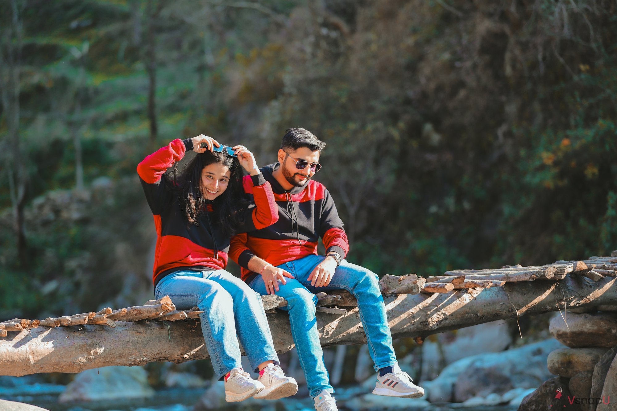 Twinning couple in matching attire sitting on a pull, surrounded by a winter wonderland and a river in the background.